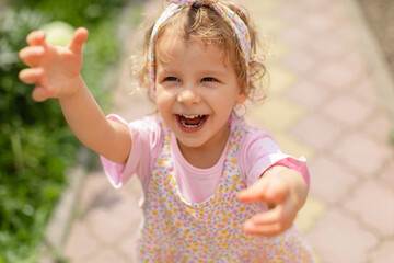 Joyful toddler girl reaching forward with a big smile while playing outdoors on a sunny day. Bright natural light, candid expression and vibrant childhood energy.