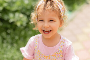 Smiling toddler girl in a floral dress enjoying a sunny outdoor moment. Bright natural light, soft background and genuine joyful expression.