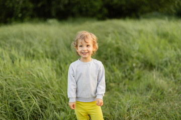 Smiling toddler standing in tall green grass on a sunny day. Warm natural light, soft background and a cheerful candid expression capturing a simple childhood moment.