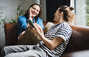 Adult lesbian couple smiling happy sitting on the sofa at home, using mobile phone