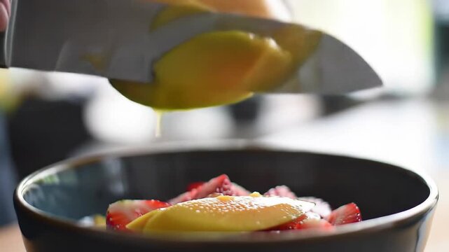 A close-up view of a refreshing fruit salad with strawberries and mangoes being added
