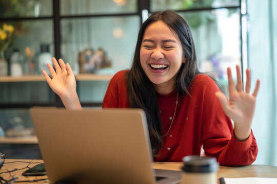 Young adult Asian woman attending a virtual team-building event, laughing while participating in an online trivia game