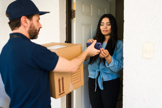 Courier delivering package to woman at front door, customer signing for online order with smartphone - Powered by Adobe