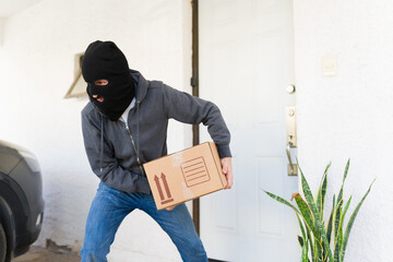 Porch pirate stealing delivery package from a home entrance, a masked thief committing a crime