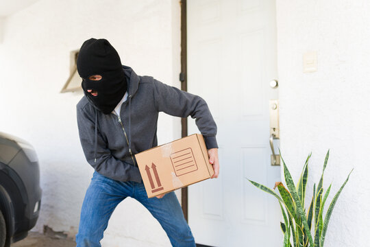 Porch pirate stealing delivery package from a home entrance, a masked thief committing a crime