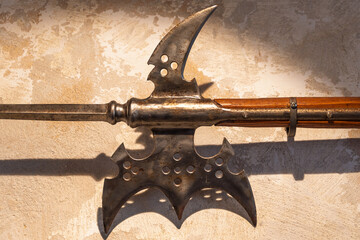 Antique halberd with weathered metal blade and wooden handle on textured wall background
