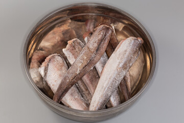 Frozen Argentine hake in stainless steel kitchen bowl, top view