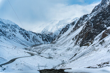 Obraz premium Scenic snowy valley with mountain pass, curving road, and winter landscape surrounded by steep slope