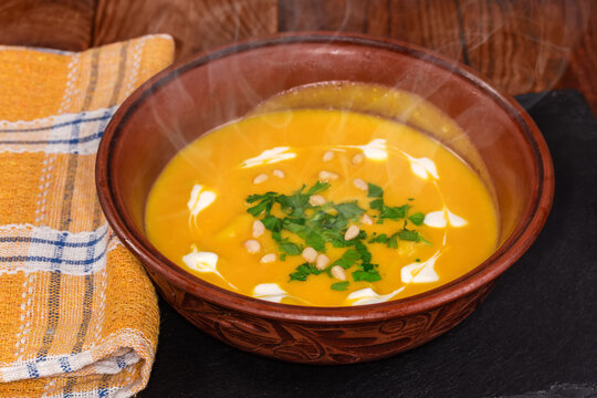 Hot lentil pumpkin soup puree in clay bowl close-up