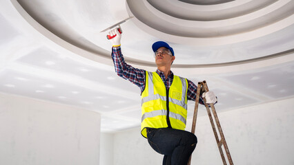 Construction worker applying finishing touches to ceiling indoor renovation site action shot bright environment upward angle craftsmanship highlight