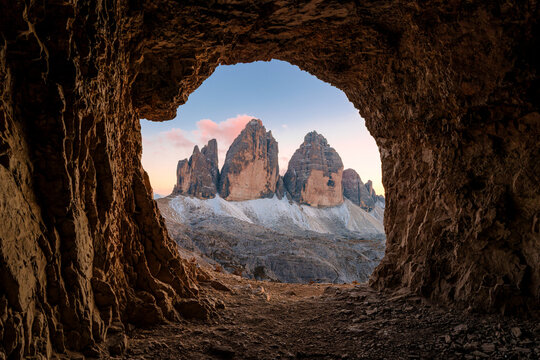 Grotta delle Tre Cime rocky tunnel framing sunset view of Tre Cime di Lavaredo mountain peak in Dolomites, Italy