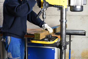 Worker using drill press to drill into wood beam in workshop