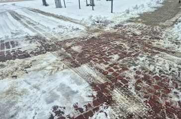 Snow-covered street with tire tracks and cleared pathways after recent snowfall. The winter scene reflects seasonal weather effects on urban environments.