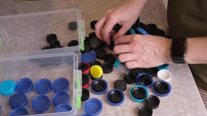 Top view of person dividing mixed pile of caps by shade, carefully moving black lids toward empty bin while blue ones stay aside, detailed look at home pre sorting before recycling center