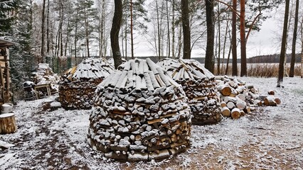 Logs sawn into decks and wood piles from chopped firewood after sanitary cutting lie on the ground near the trees. They are designed for heating houses. Everything is covered with snow. Cloudy winter