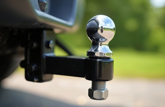 Shiny chrome trailer ball hitch closeup on car. Black tow bar mounted to vehicle rear for hauling. Towing equipment used to pull boat cargo camper. Metal hook connection for transport travel, road