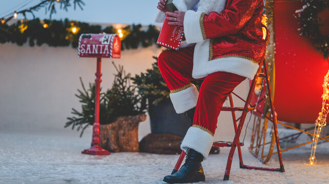 Santa Claus reading letters near a mailbox on a snowy Christmas Eve