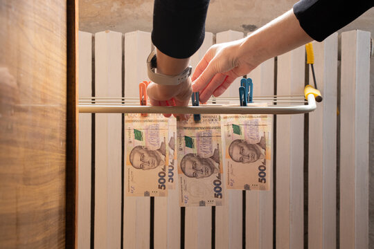 There is a central heating radiator in the apartment and a hanging dryer, on which a woman hangs Ukrainian banknotes with clothespins, creating an image of high tariffs, costs for heating - Powered by Adobe
