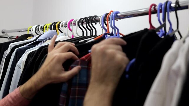 A man is rummaging through things on a hanger in a wardrobe.