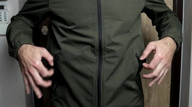 A man in a soft green jacket quickly checks his pockets, sleeves and zippers with his hands before leaving.