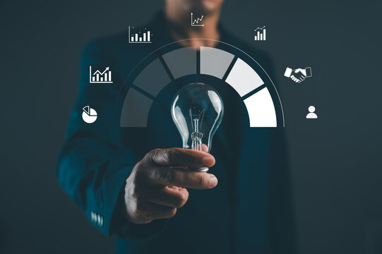 A businessman holds a light bulb in front of a digital dashboard with graphs, representing innovation and data analysis.