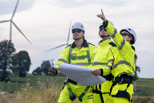 Construction team reviews plans while overseeing wind turbine installation at a renewable energy site in daylight - Powered by Adobe