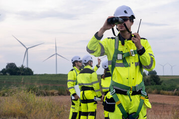 Team of workers inspecting wind turbines during a cloudy day in a renewable energy field