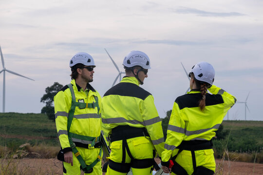 Workers in safety gear discussing wind turbine installation at a renewable energy site in the countryside during the late afternoon - Powered by Adobe