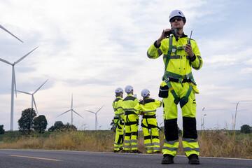 Team of workers in bright safety gear inspecting wind turbines at a renewable energy site on a...