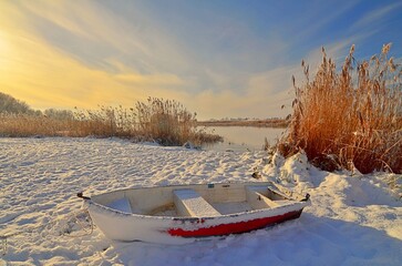 frozen boat on the river at winter sunset