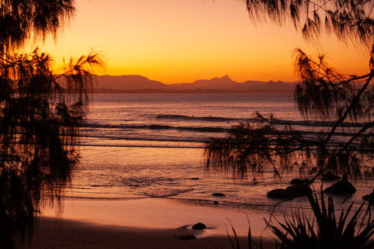 Ausblick auf das Meer und den Strand von Wategos Beach bei Sonnenuntergang. Mt. Warning, Wollumbin im Hintergrund des roten Sonnenuntergangs am Strand.