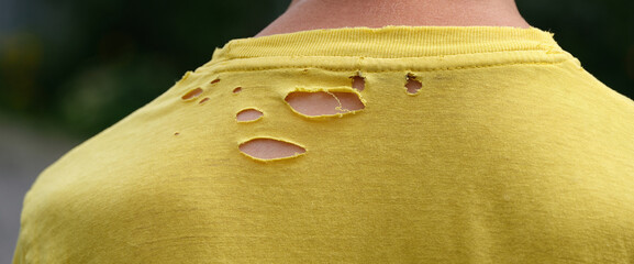 A close up shot of the back of a man wearing an old yellow t-shirt with holes in it. Close up.