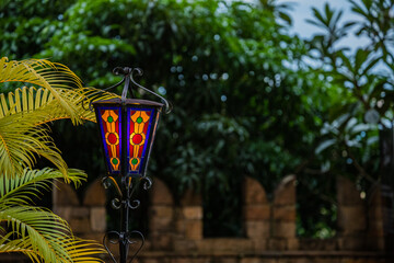 A lamp post with a green and yellow lampshade is in front of a wall