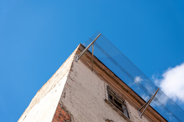 Old damaged building facade with broken windows and protective metal mesh installed above to prevent falling debris and ensure safety during planned renovation.