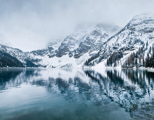 Snowy mountain lake with still reflections and misty cold alpine scenery