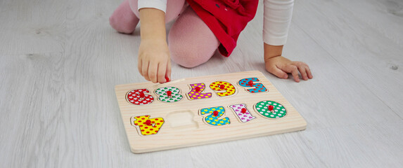 Toddler girl playing with a wooden educational puzzle and sorting shapes on the floor at home.