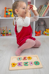 Toddler girl playing with a wooden educational puzzle and sorting shapes on the floor at home.