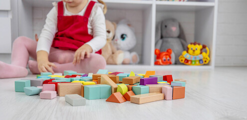 Little girl building a tower with colorful wooden blocks on the floor.