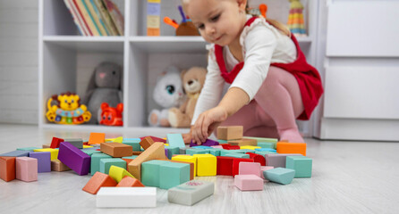 Little girl building a tower with colorful wooden blocks on the floor.