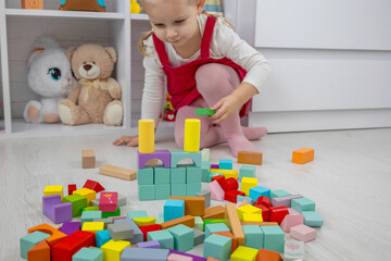 Little girl building a tower with colorful wooden blocks on the floor.