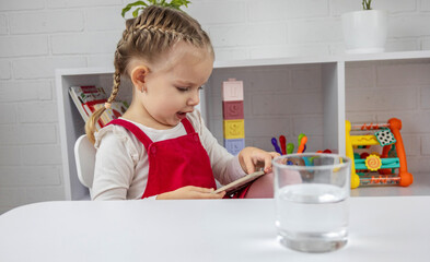 A glass of clean water on a table in the foreground, and a child reading in the background.