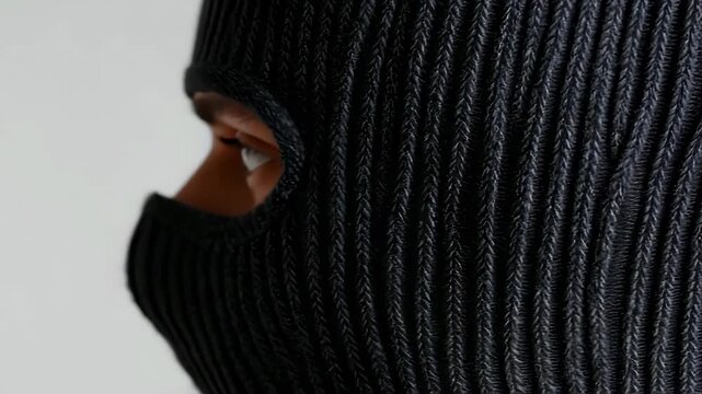 Close-up of a person's intense eyes visible through a black knit balaclava, creating a mysterious and confrontational atmosphere.