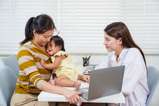 Pediatrician talking with mother holding toddler after health examination using laptop to review result representing care professionalism and family trust in pediatric healthcare