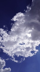 Dramatic photograph of white fluffy cumulus clouds against a deep navy blue sky, ethereal concept.