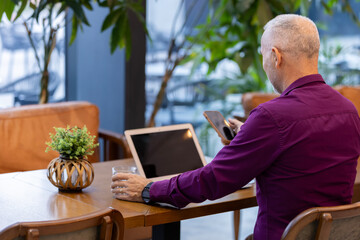 Senior man using smartphone in modern cafe