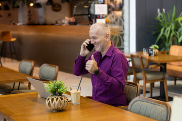 Mature man talking on phone giving thumbs up in cafe