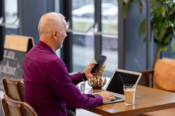 Mature man working remotely using laptop and smartphone