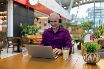 Mature man working on laptop in cafe wearing headphones
