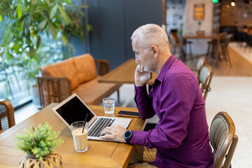 Mature man working on laptop in modern cafe