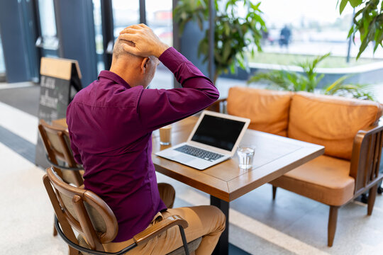 Stressed man experiencing headache touching head at cafe